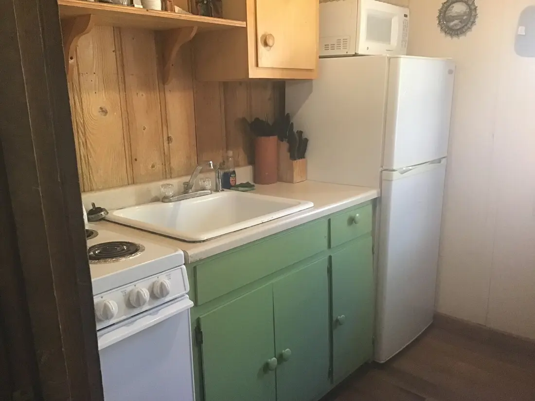 The kitchen — white gas range, deep sink under the window, mint-green cabinets and a full-size refrigerator.