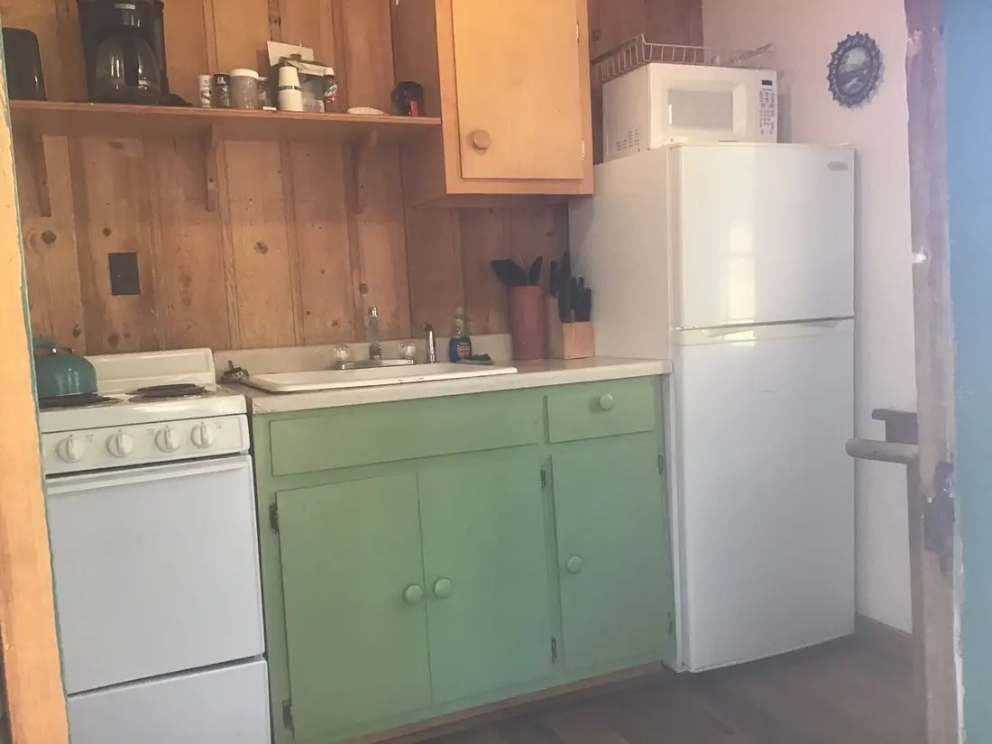 The kitchen from the doorway — range and sink along the wall, microwave above the refrigerator, coffee pot and mugs on the shelf.