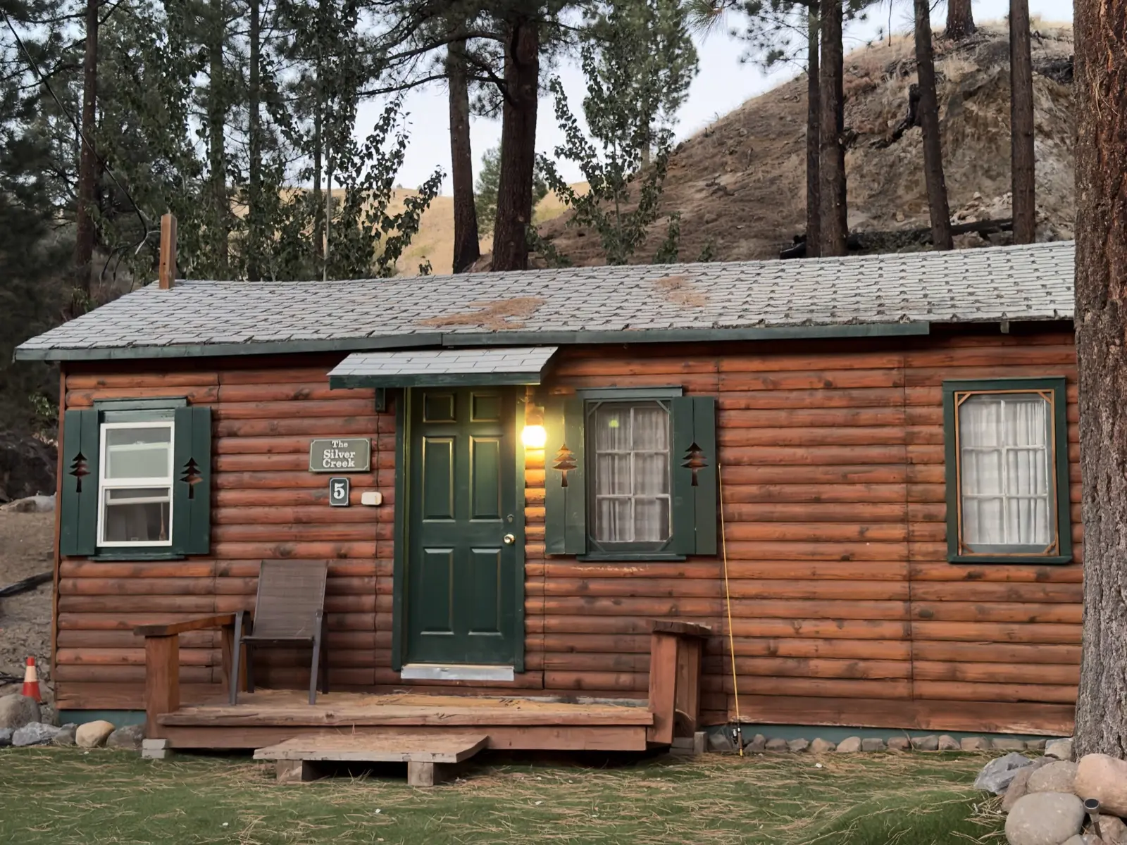 Cabin №5, Silver Creek — square on at dusk, the porch light lit and the nameplate beside the door.