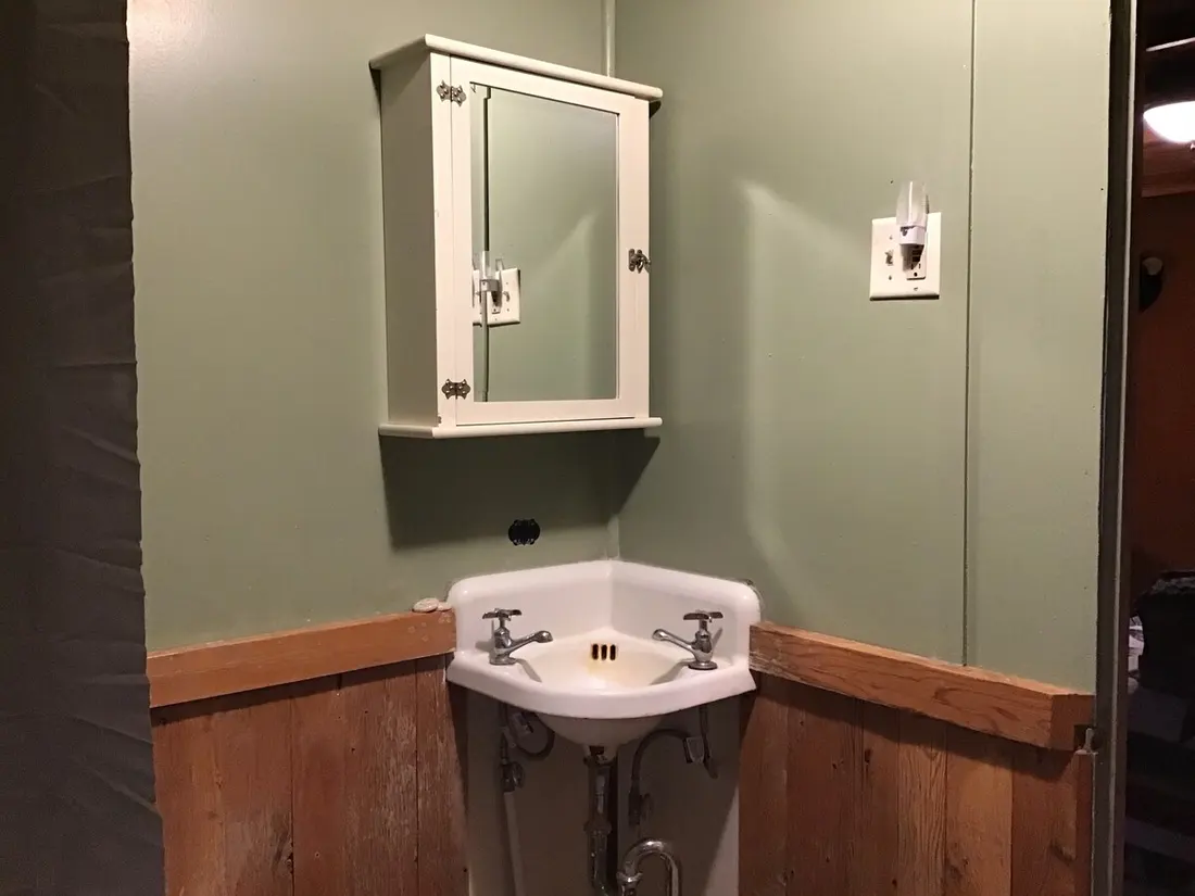 The bathroom sink beneath a mirrored medicine cabinet, wood wainscot below sage-green walls.