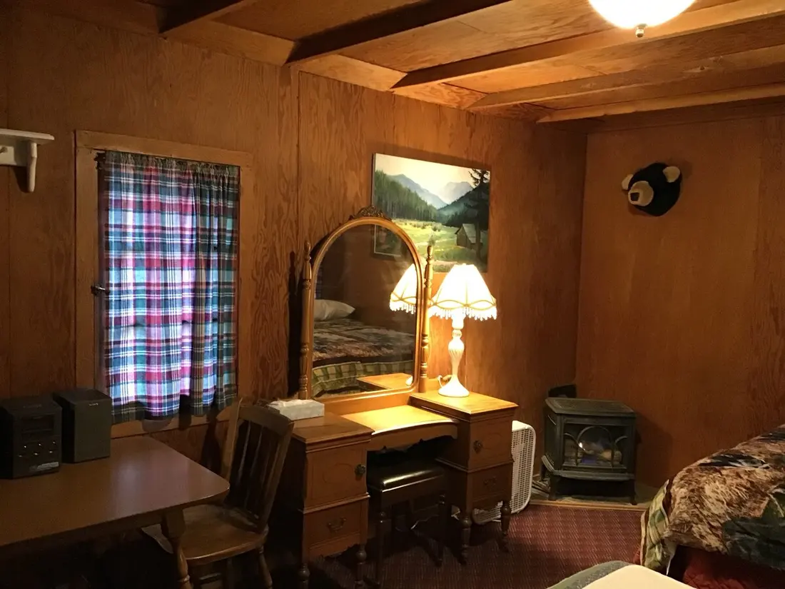 The sitting area — A writing desk and mirror with the wood stove in the corner, a framed landscape above.