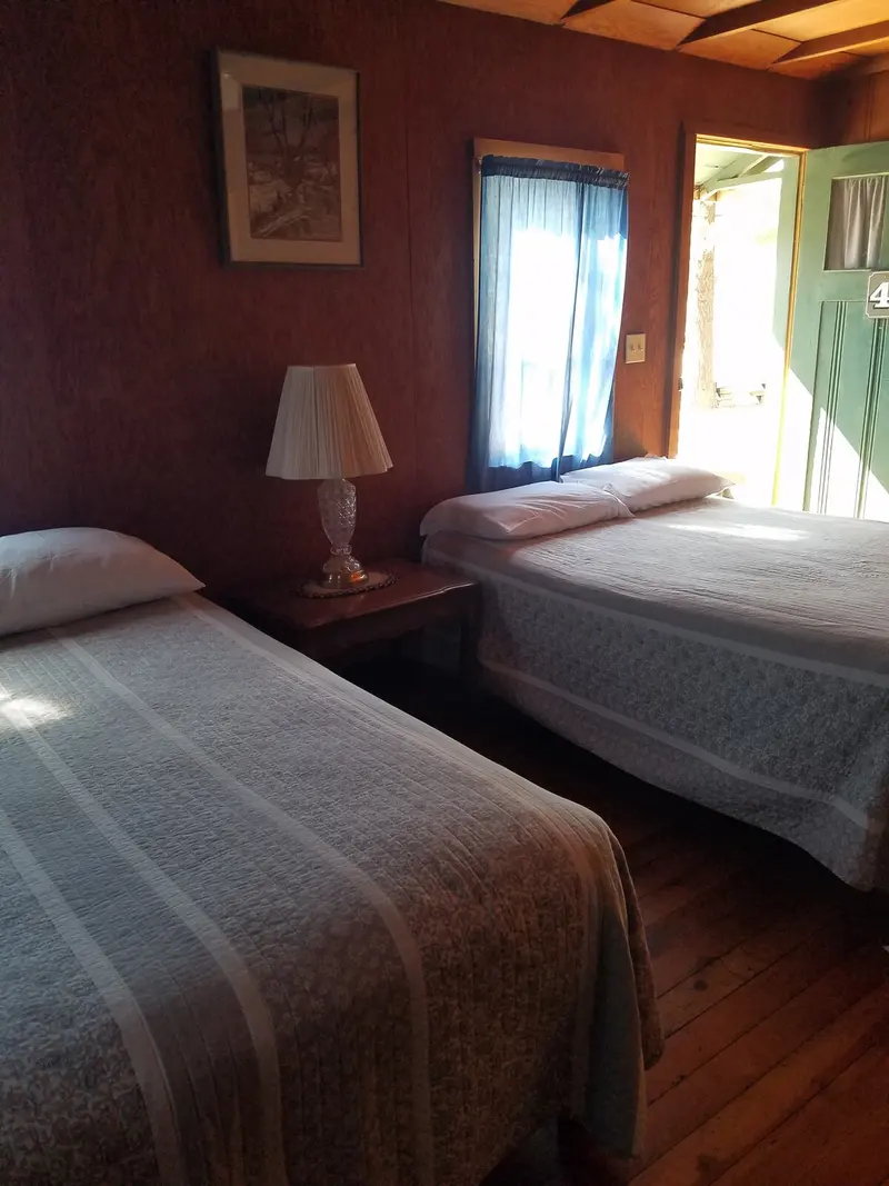 The bedroom from the doorway — two beds, a lamp on the nightstand, the numbered door open to the outside.