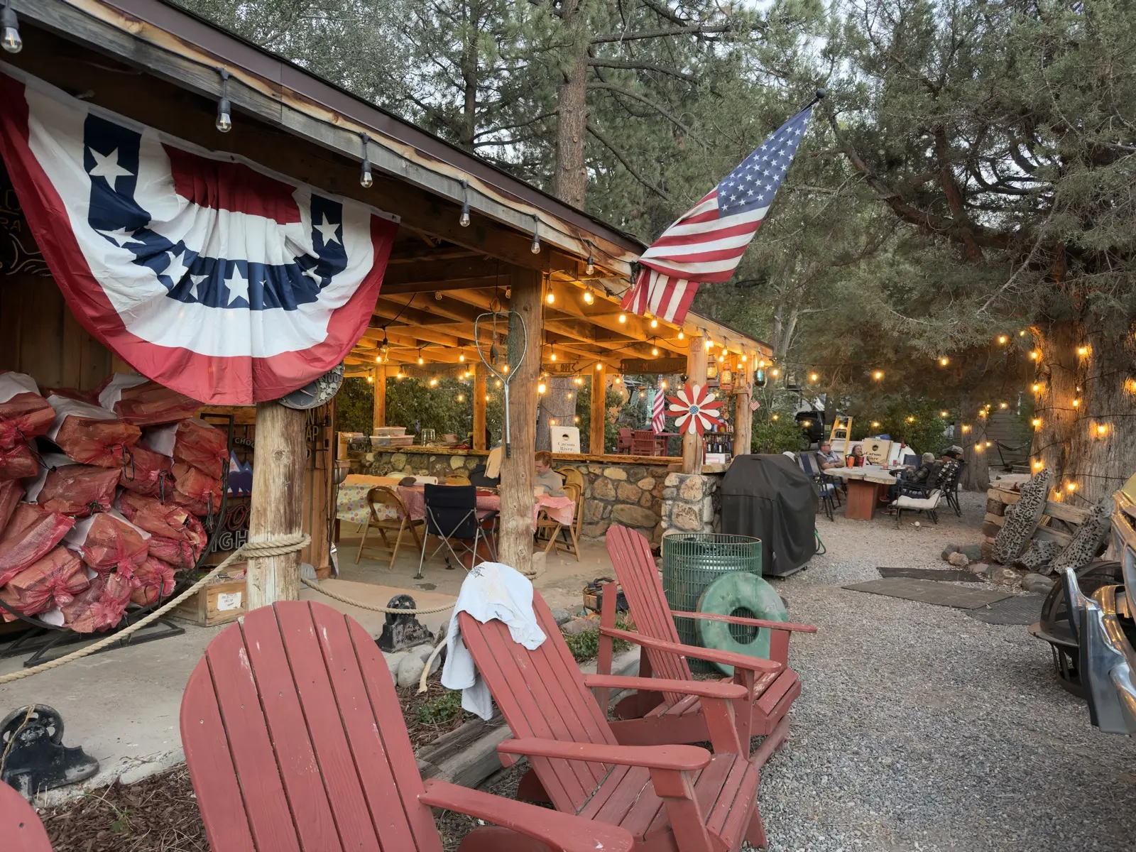 The covered side patio — the grills and the firewood under its roof, the bunting up for the Fourth.