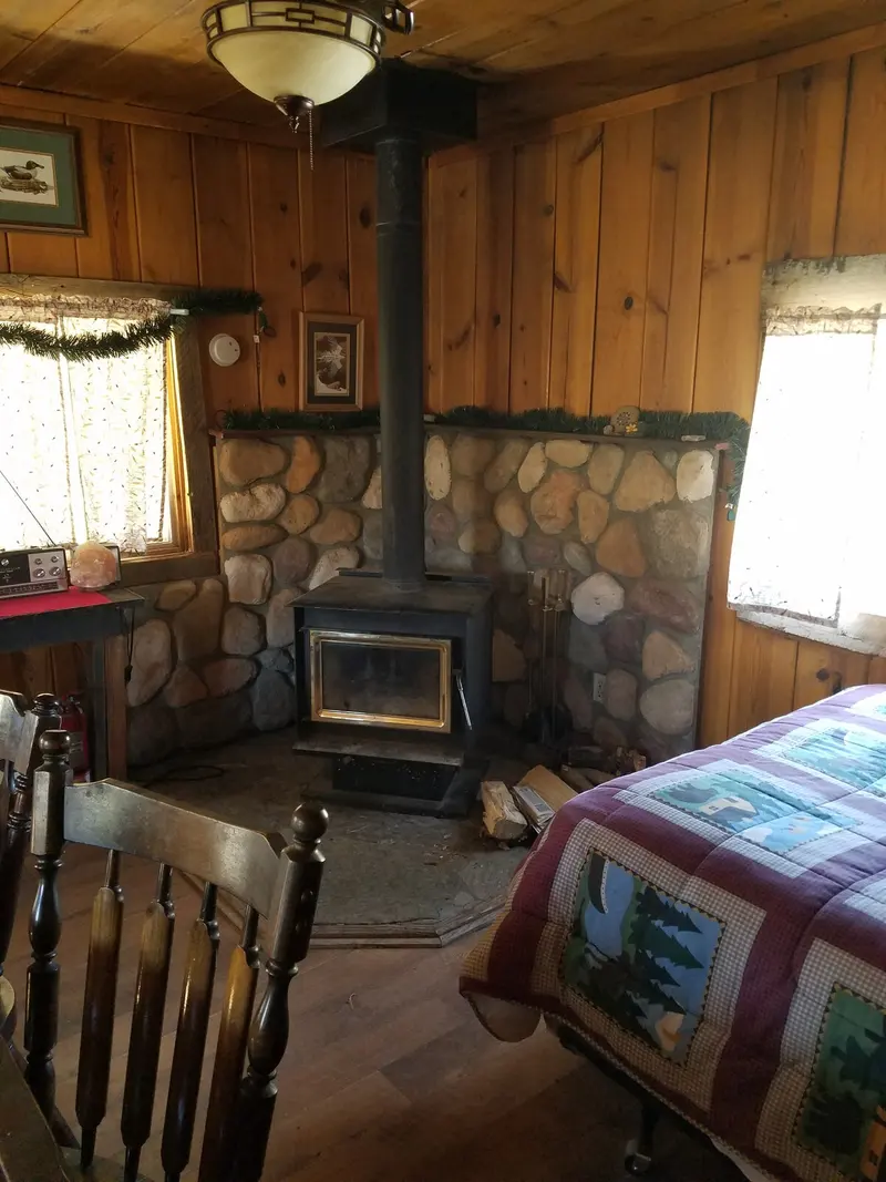 The beds — A bed beside the river-rock hearth and its wood stove, curtains at the windows.