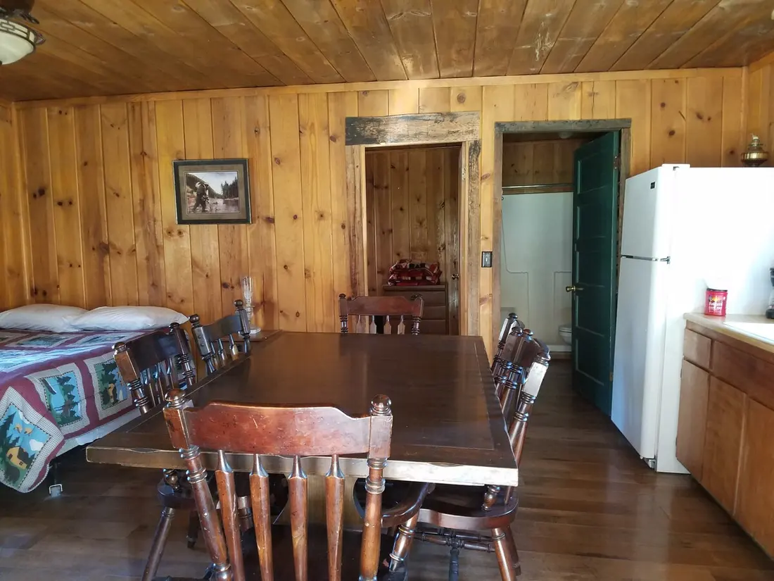 The dining room — The long dining table with eight chairs, the counter and refrigerator beyond, doorways to the rest of the cabin.