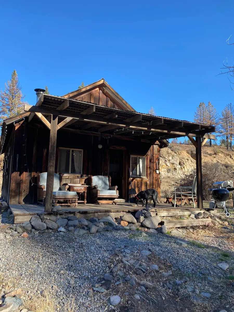 The River Cabin — cabin №7, its deep covered porch and armchairs above the river rock, a dog on the deck.