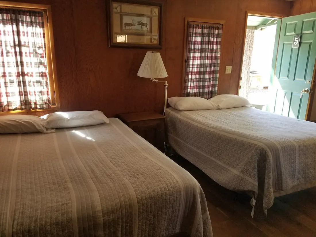 The bedroom — Two beds under plaid curtains, a lamp between them, the green door with its 5 standing open.