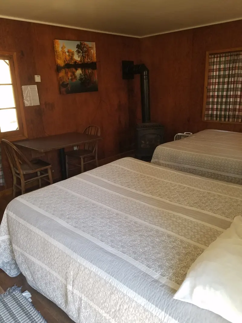 The bedroom — The room from the bed — a dining table and chairs by the window, wood stove against the wall.