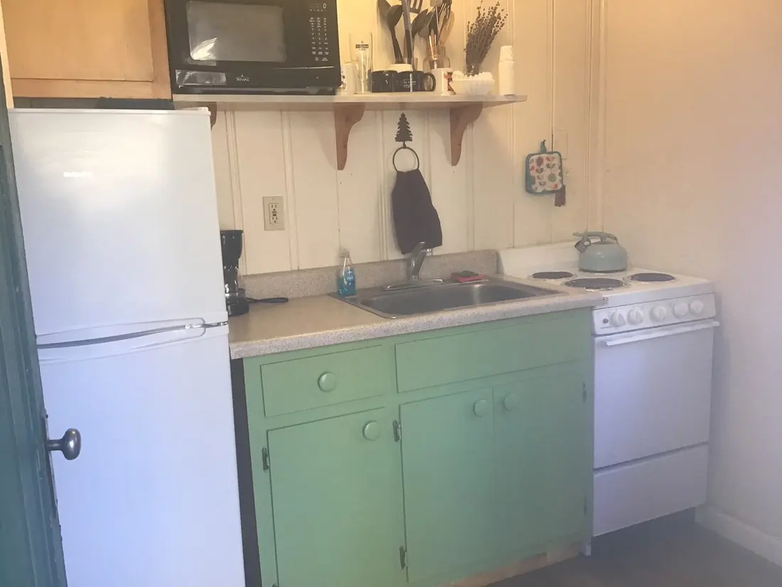 The kitchen — microwave on the shelf above, refrigerator alongside, sink and electric range with a kettle on it.