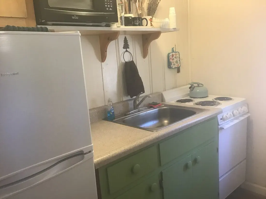 The kitchen counter — sink and range, mint-green cabinets below, mugs and coffee things on the shelf above.