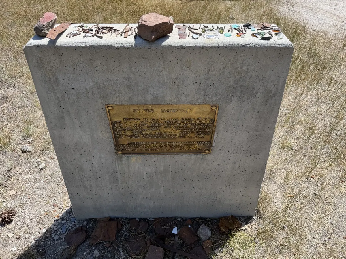 The Silver Mountain marker on Highway 4 — square nails and glass left as offerings on its cap.