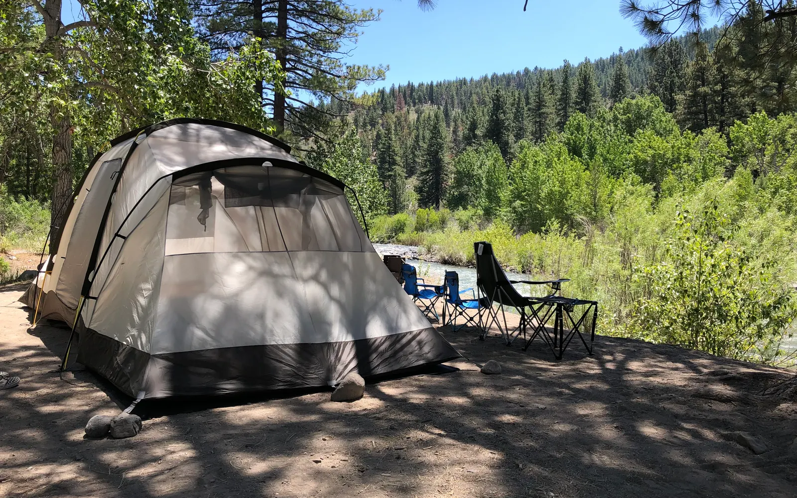 A riverside tent site under the pines, camp chairs facing the East Fork — the owner's photograph, July 2019.