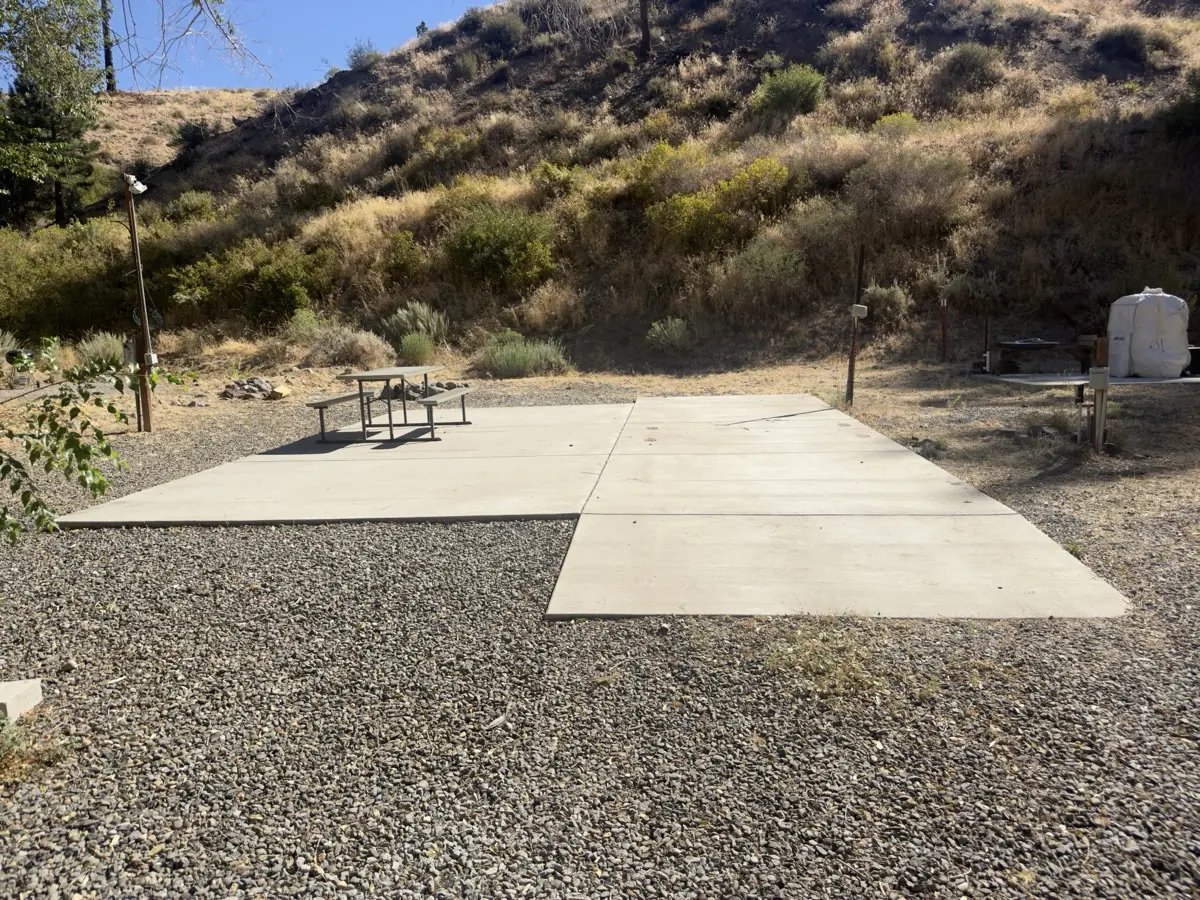 One of the up-top spaces — a level concrete pad with its own table and hookup post, the hill behind; the resort's own photograph, September 2026.