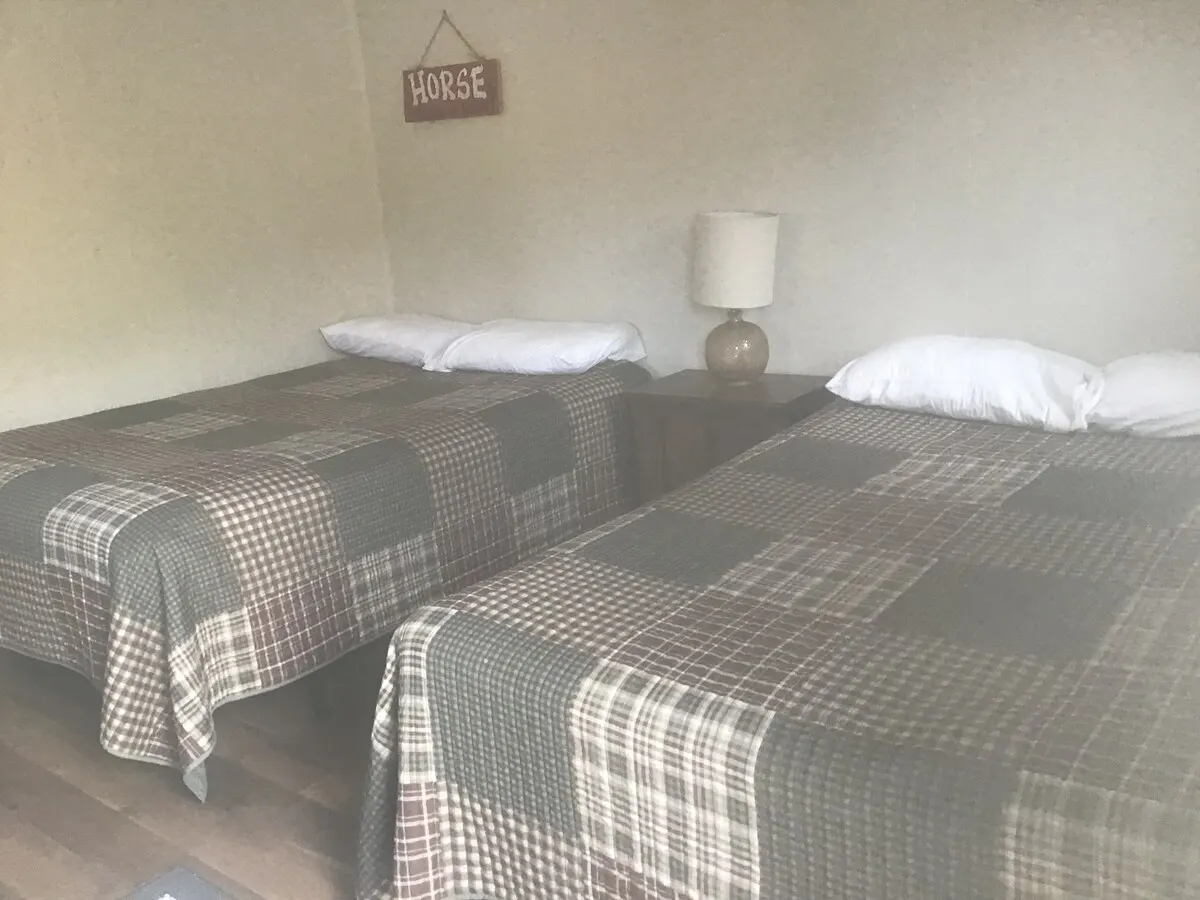 The bedroom — Both beds from the door, a lamp on the nightstand between them, the HORSE sign on the wall.